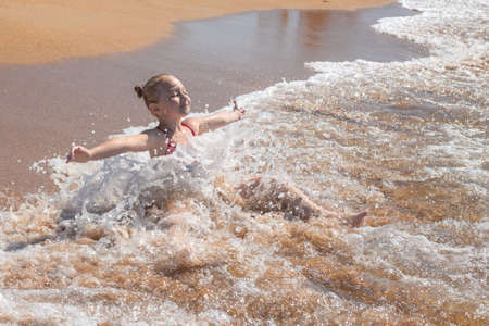 A little girl bathes in sea water on a sandy shore. Summer vacation at the sea.の写真素材