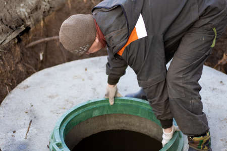 A man installs a sewer manhole on a septic tank made of concrete rings. Construction of sewer networks in the village.の写真素材