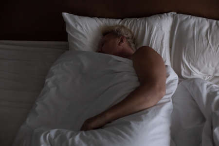 Mature sleeping man in his bed with white sheets. Good rest and healthy sleep at night.の写真素材