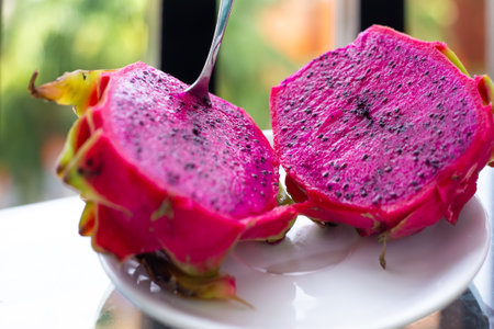 A red-fleshed dragon fruit cut in half with a spoon stuck in. exotic tropical fruits.の写真素材