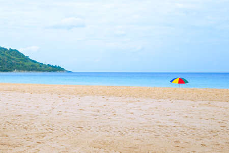 Empty sandy beach with bright umbrella and mountain. Travel and tourism.の写真素材