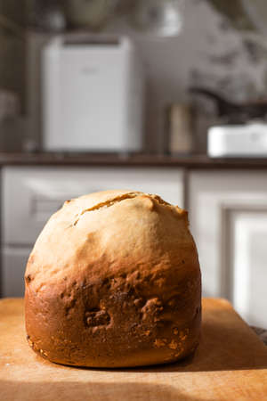 A loaf of fresh fluffy homemade bread baked in a bread machine, lit by the sun against the backdrop...