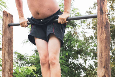 An elderly man in shorts and with a belly goes in for sports, on the horizontal bar. Active...