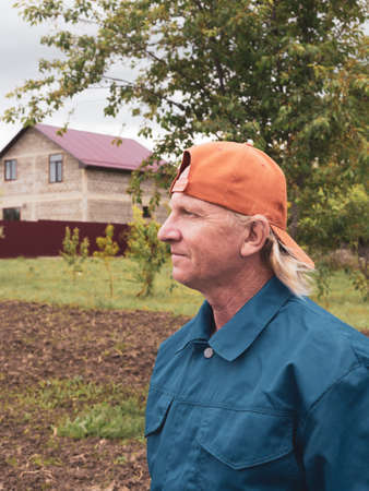 Mature male farmer on the background of the house and garden. Farming and growing plants.の写真素材
