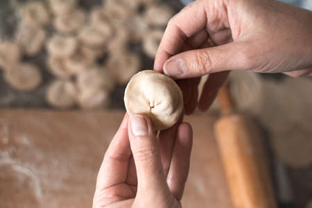 A woman sculpts dumplings from dough with meat filling in the kitchen. Cooking delicious homemade dumplings.の写真素材