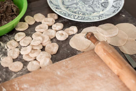 Preparation of dumplings. Meat filling in a cup, dough dumplings and a board with a rolling pin.