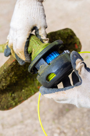 The gardener puts the trimmer head on the mower. Replacing the line on a lawn mower.