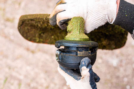 A gardener removes a trimmer head from a lawn mower to thread line. Spring grass moving.
