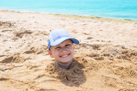 the boy's head sticks out of the sand. Fun weekend at the seaside.の写真素材