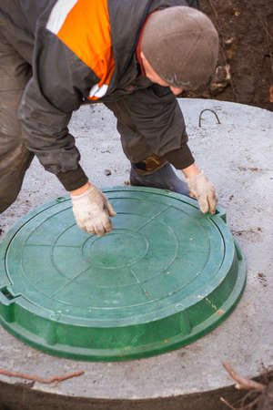The plumber lifts the cover of the sewer well for maintenance. Cesspools and septic tanks in the courtyard of the house.の写真素材