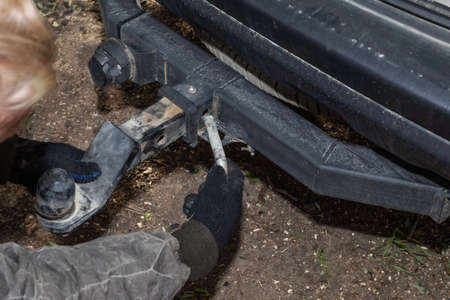 A man mounts an iron towbar on a car for towing a trailer. Device for transportation.