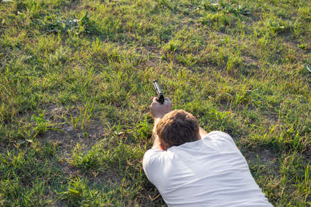 A man with a pistol, lying on the grass, aims for a shot. copyspace.の写真素材