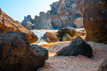 Rocky grotto on the sea coast with splashes of breaking waves on the rocks.
