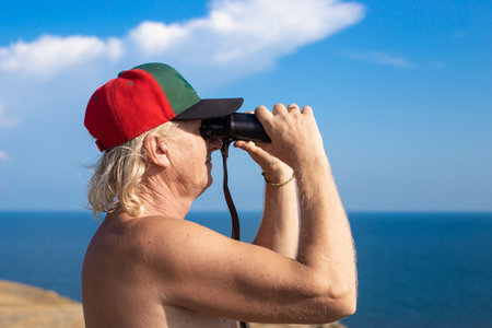 Adult A man with binoculars looks at the sea in the distance, on a summer sunny day. close up.