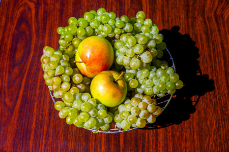 Green grapes and apples in a fruit bowl on a wooden table, top view. Fresh fruit, still life.