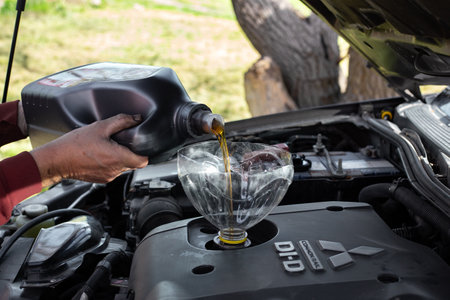 A man pours Mobile machine oil through a funnel into the engine of a Mitsubishi car. Car maintenance by himself. Russia, Anapa-25.04.2022のeditorial素材