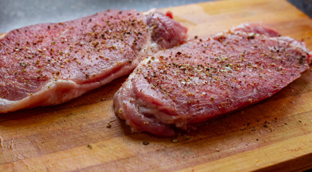 Pieces of raw meat sprinkled with salt and spices on a cutting board. Cooking pork steaks chops.の写真素材