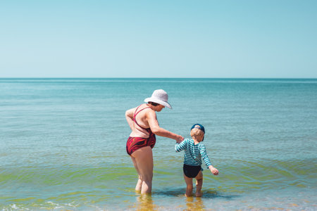Grandmother and grandson go into the sea for swimming. Summer holidays on the sea coast with the whole family.の写真素材