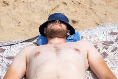 a large man in a Panama hat with white skin and a red beard is sunbathing on the beach on a sunny day. Rest and relaxation.の写真素材