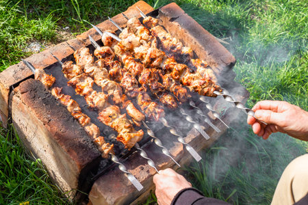 man cooks a juicy meat kebab on a homemade grill, turning the skewers. Village spring picnic, fried shish kebab.の写真素材