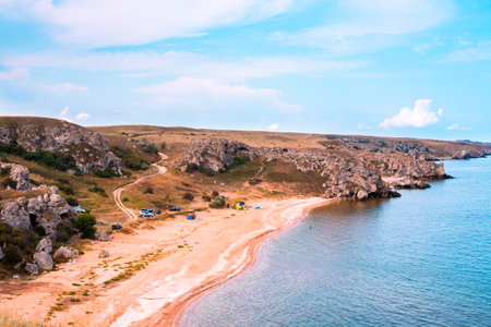 Sea bay with sandy shore and hills. Tourists and travelers rest on the shore in a tent camp.の写真素材