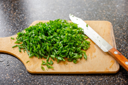 Green fresh onion feather cut on a wooden board. Summer cooking ingredient.