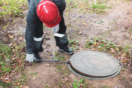 a man in overalls opens a sewer hatch. Cleaning of sewers and drains.の写真素材