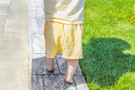 a small child runs barefoot along the curb on the lawn, rear view. Baby's first steps.