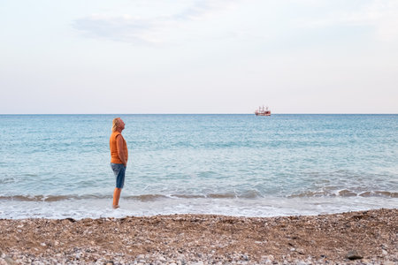 Mature Caucasian blond man stands on the seashore and looks at a sailing ship.の写真素材