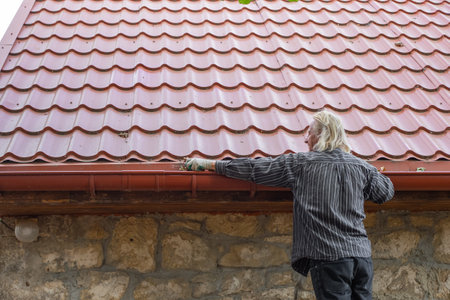 A mature man removes leaves and debris from the gutter of his house. Cleaning a rain drain.の写真素材