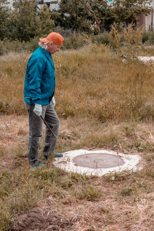 A working man with a crowbar stands near a well. Inspection of wells, septic tanks and water wells.