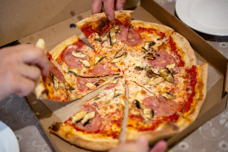 large pizza on the table in a box, cut into pieces, which people take with their hands at the feast.の写真素材