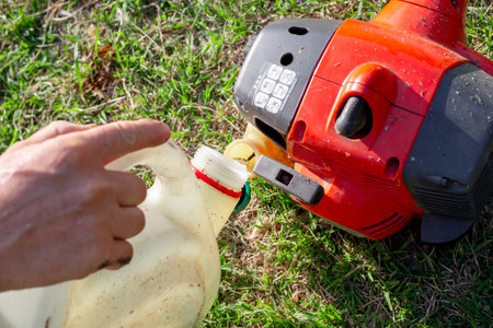 A gardener fills a lawn mower with a mixture of gasoline and oil. Maintenance of garden equipment.