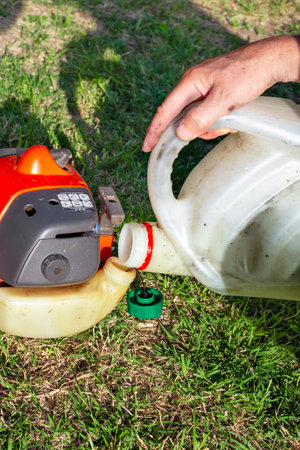 gardener fills a lawn mower with a mixture of gasoline and oil. Maintenance of garden equipment.
