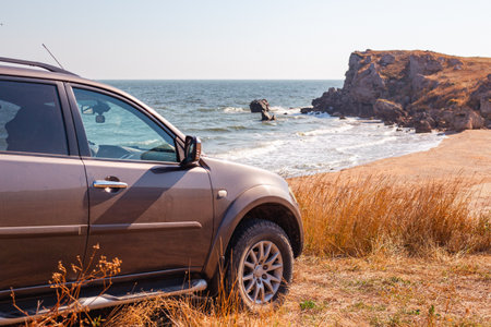 SUV car on the rocky sea coast with a sandy beach and sun-scorched grass. Travel and tourism.の写真素材