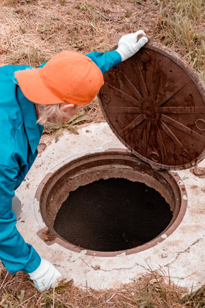 A worker holds a well manhole cover. Open the well. Plumbing work in rural areas.