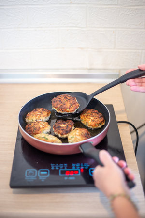 Cooking. The frying pan is on the induction stove, the hostess is turning the meat patties over to...