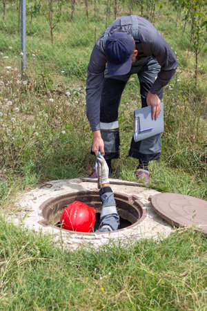 Plumbers repair pipes in a well. A man hands a wrench to a worker in the well.
