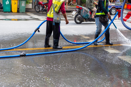 Workers in rubber boots with hoses in their hands wash the road surface with water.の写真素材