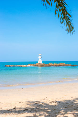 White lighthouse on rocky shoal in sea on tropical coast. Vertical Seascape.の写真素材