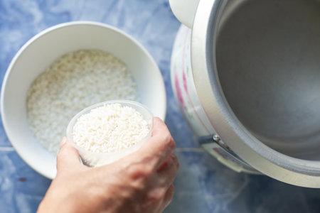 Cooking rice in a rice cooker. The woman measures out a cup of rice and pours it into a cup.の写真素材