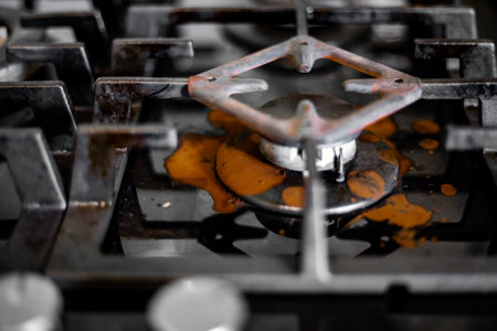 An extinguished gas burner with a coffee maker stand and spilled brewed coffee on the stove surface.の写真素材
