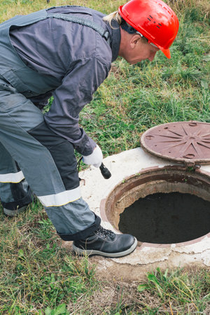 A worker in a helmet with a flashlight inspects an open well. Maintenance of water wells, septic tanks, meters and pipes.の写真素材