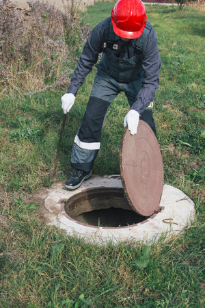 Worker opens septic well manhole cover. septic tank maintenance and sewage pumping.の写真素材