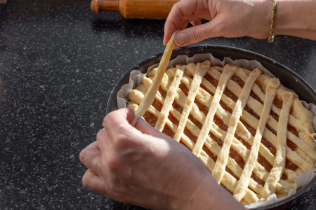 Making a Sweet Jam Pie, laying out strips of dough in a lattice pattern over the sweet filling, viewed from above.の写真素材