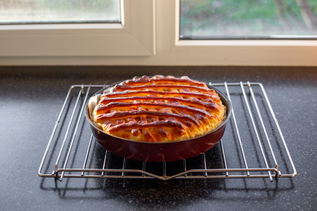 A rich pie with jam, the top crust is made of woven dough in a lattice pattern. Delicious pastries on the kitchen countertop near the window.の写真素材