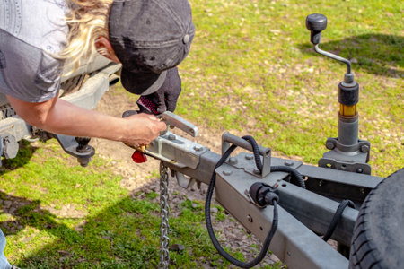 A man hits a trailer to a car by unlocking the anti-theft lock on the trailer's drawbar.