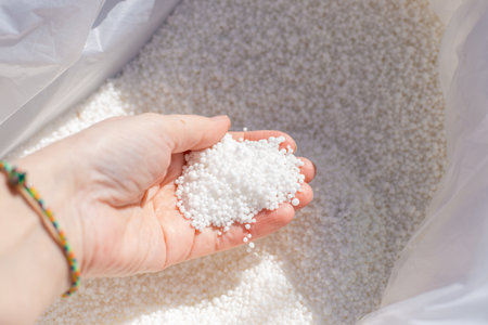 A woman's hand holds granules of mineral fertilizer taken from a bag. Nutrition and fertilizing of...