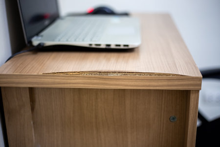 Workplace with laptop on a chipboard table with a delaminated edge due to humidity. Care of wooden surface.の写真素材