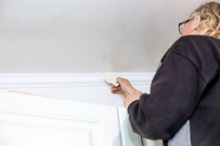 A person uses a rubber spatula to fill the joints on the ceiling after installing skirting boards....
